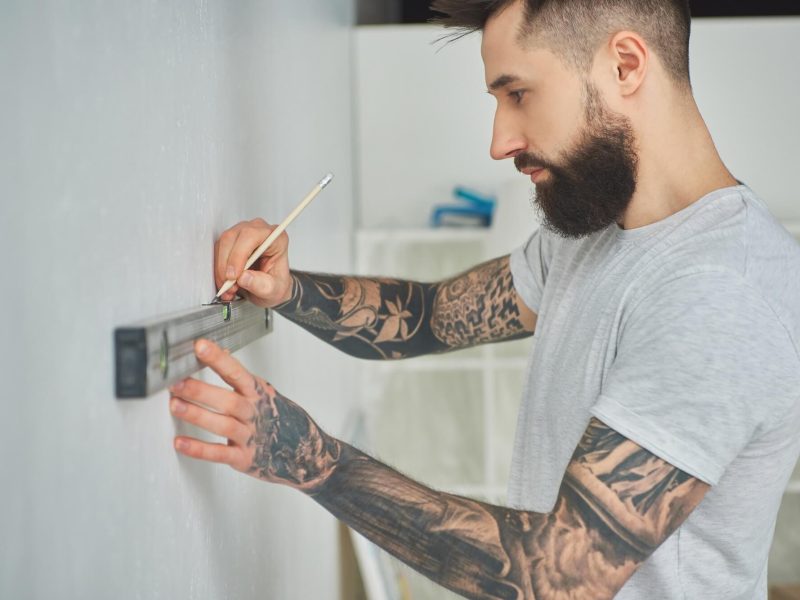 side-view-of-handsome-bearded-young-man-holding-level-tool-and-pencil-during-home-improvement.jpg